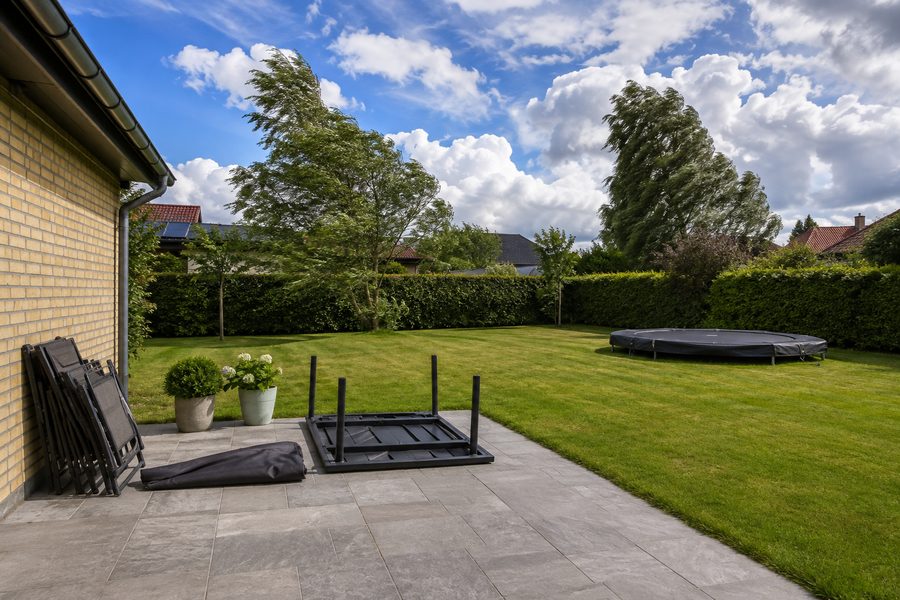 Een achtertuin voor de storm: tuinstoelen ingeklapt tegen de gevel, de parasol neergelegd en de tafel omgekeerd op het terras